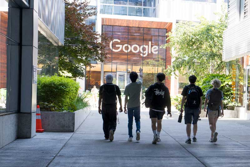 Five Northeastern students walk toward a building with a Google sign above the entrance as the student second from left points at the building